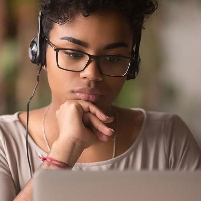 Student studies her laptop while wearing headphones.